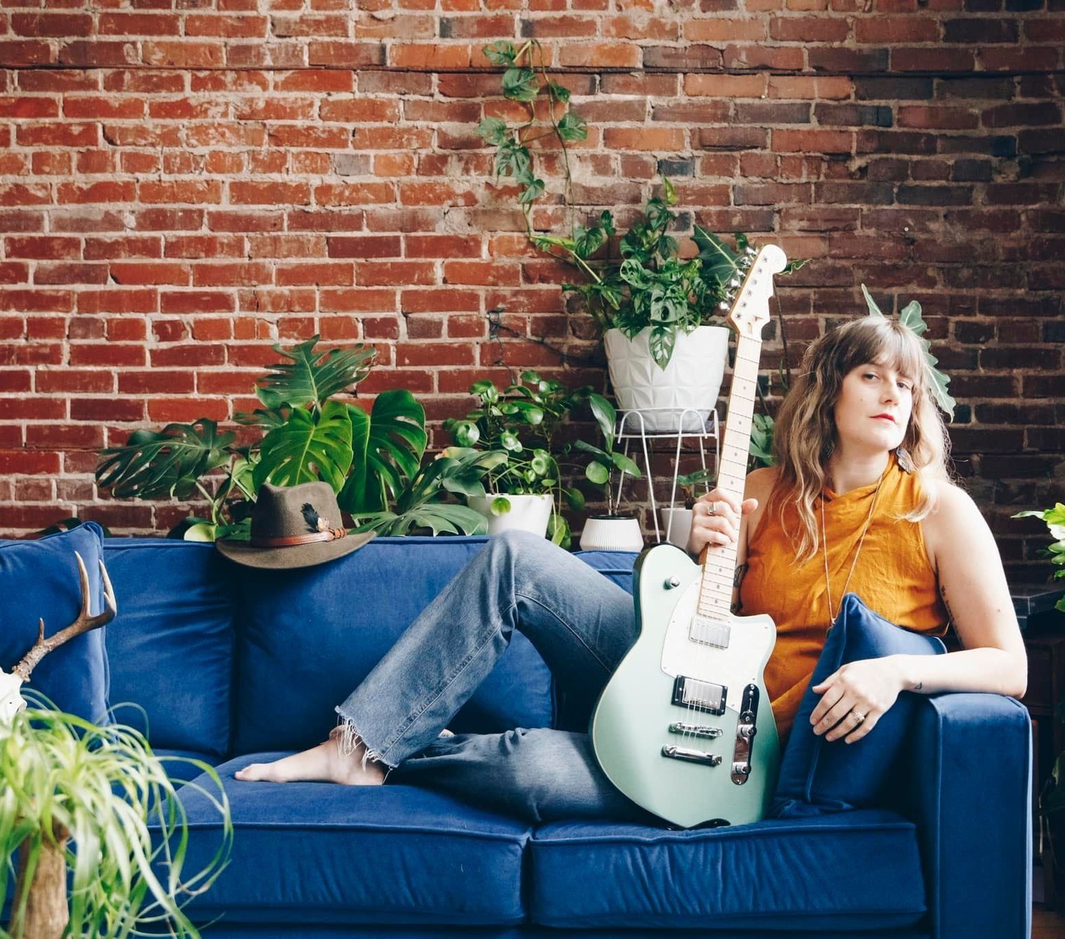 Woman posing on a blue couch with an electric guitar