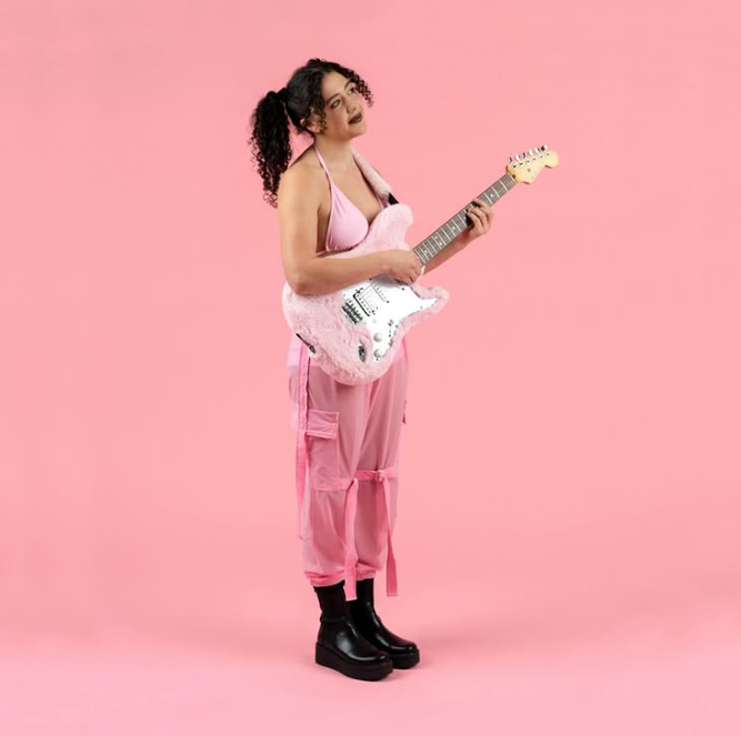 Girl wearing all pink holding a pink electric guitar